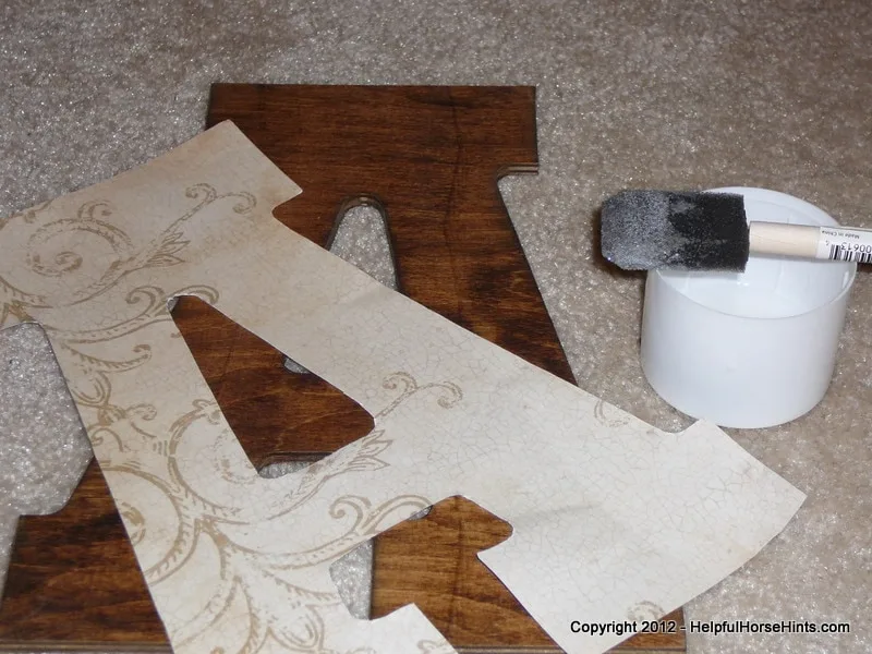 prepping modpodge and other supplies to adhere decorative paper to diy horse stall sign.