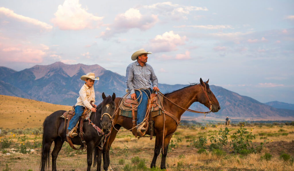 A cowboy and his son on horseback looking over ranch 