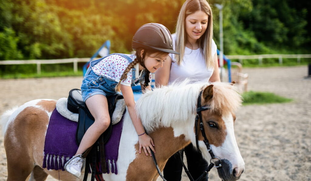 A little girl enjoys riding on the back of pony 