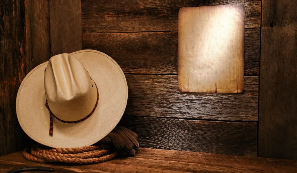 American west rodeo cowboy white straw hat and authentic western rope on weathered wood floor in an old barn