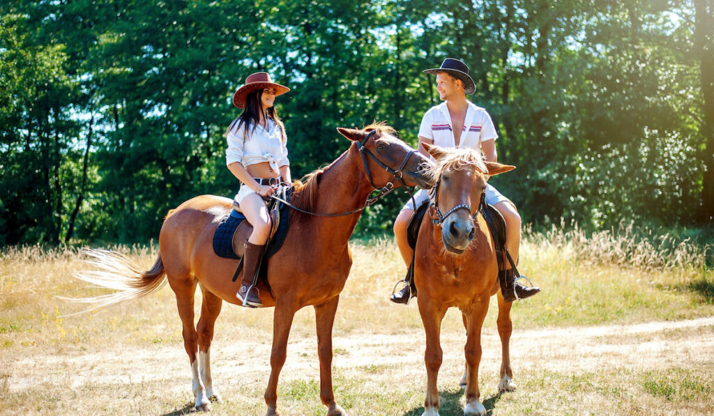 Beautiful couple horseback riding in nature on a bright sunny day
