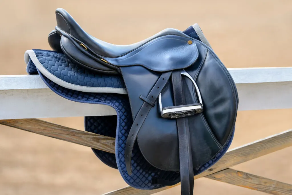 Black english saddle hanging on fence near stables 