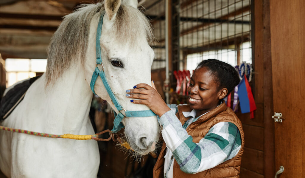 Broodmare Manager stroking her white horse in stables