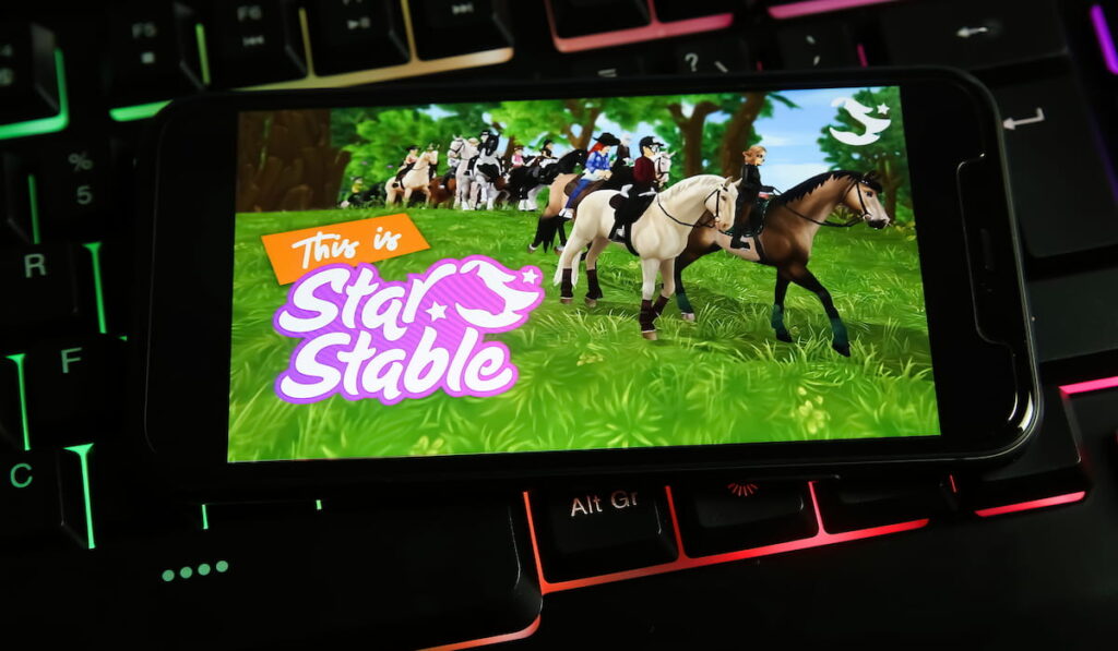Closeup of mobile phone with logo lettering of pc game starstable on computer keyboard 