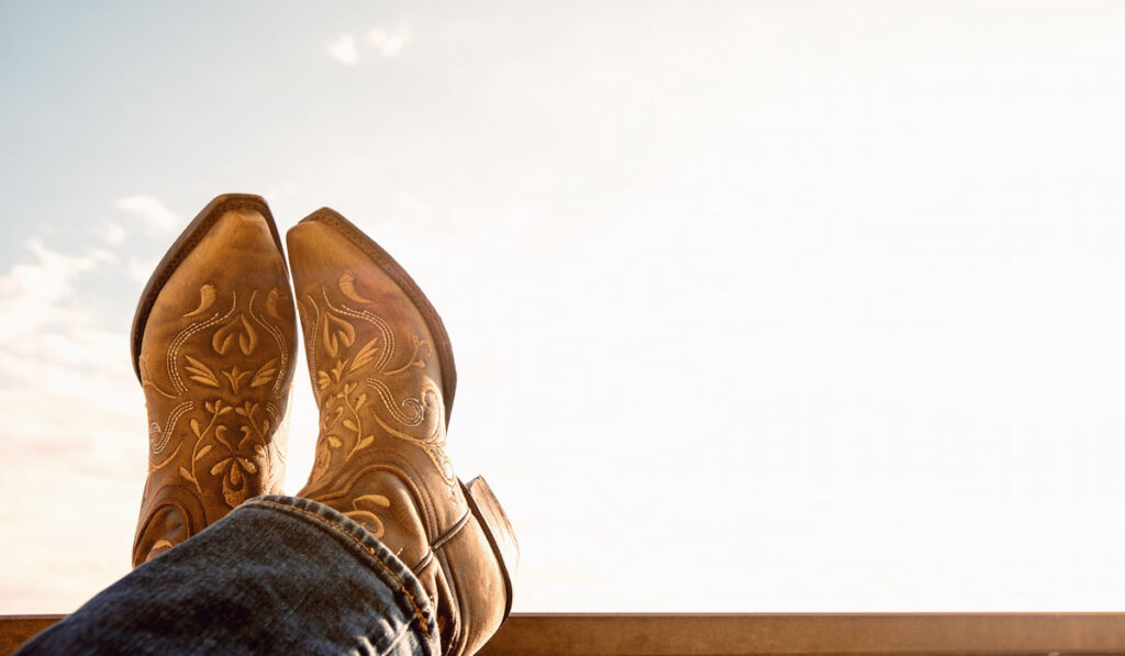 Cowboy resting legs with feet crossed, sky background and showing a toe cowboy boots