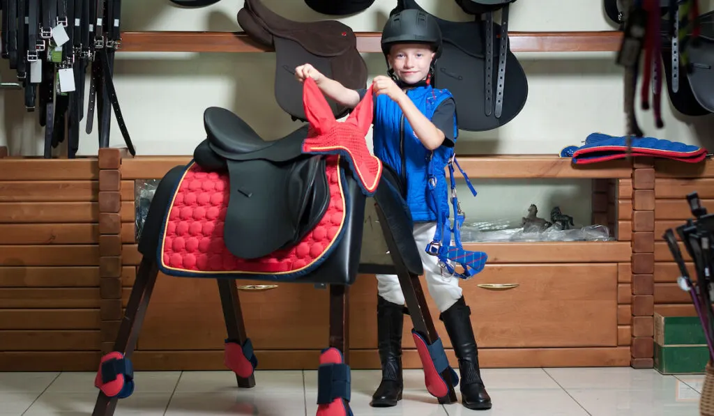 Cute little boy in equestrian shop with saddle beside him