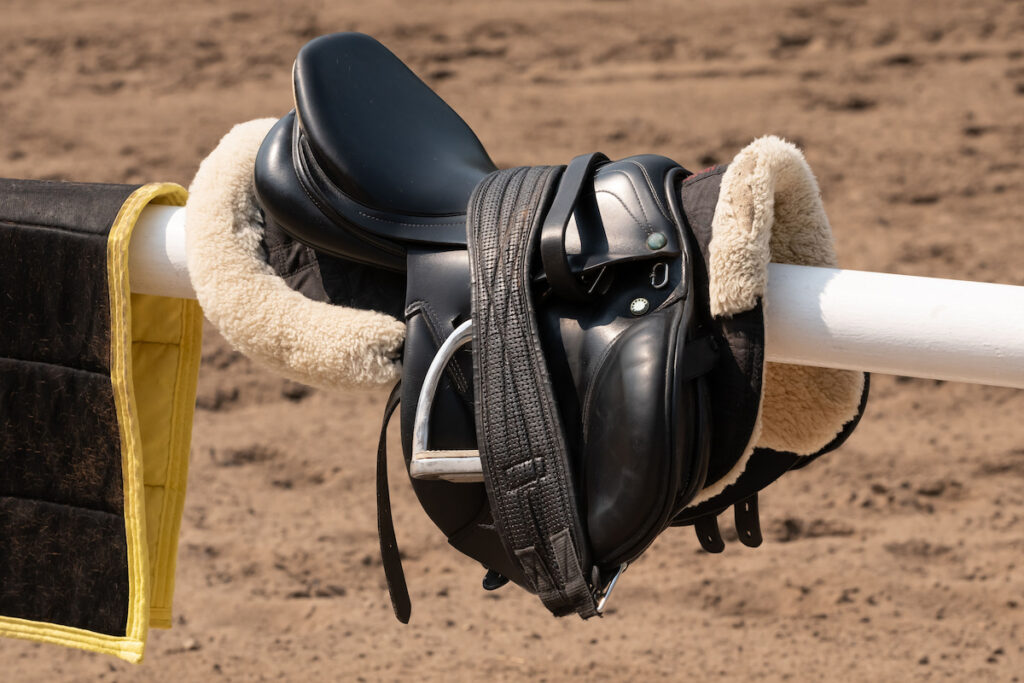 English saddle and bridle hanging on white wooden stable