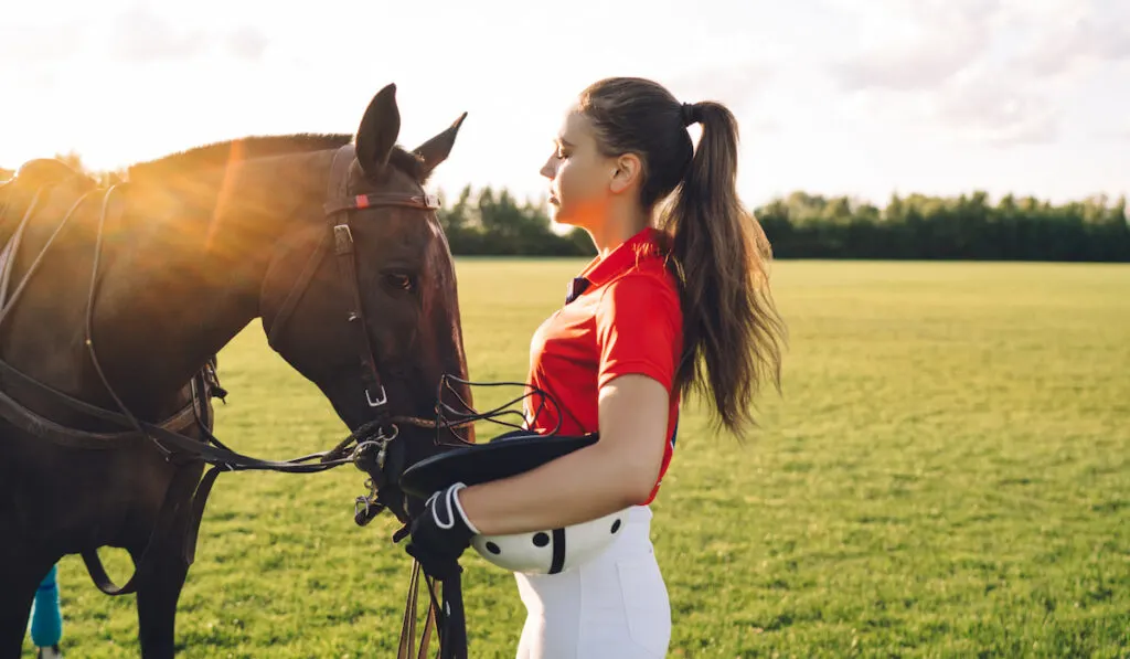 Female Equestrian caressing horse on green field