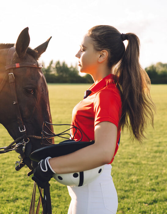 female equestrian caressing horse on green field