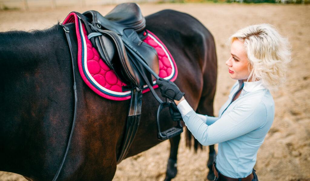 Female blonde preparing a horse saddle on her black stallion
