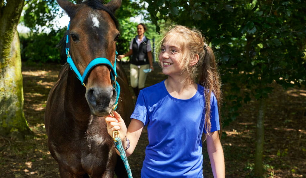 Girl holding lead rope looking at horse 