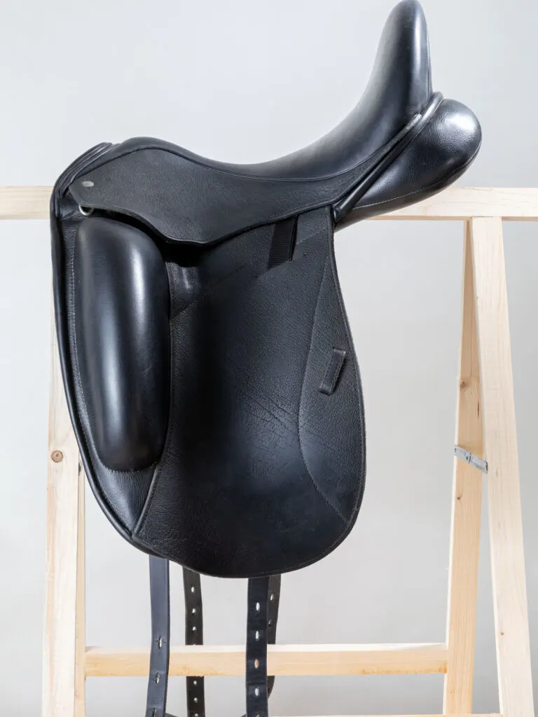 Leather black flap dressage horse saddle on a wooden rack on white background