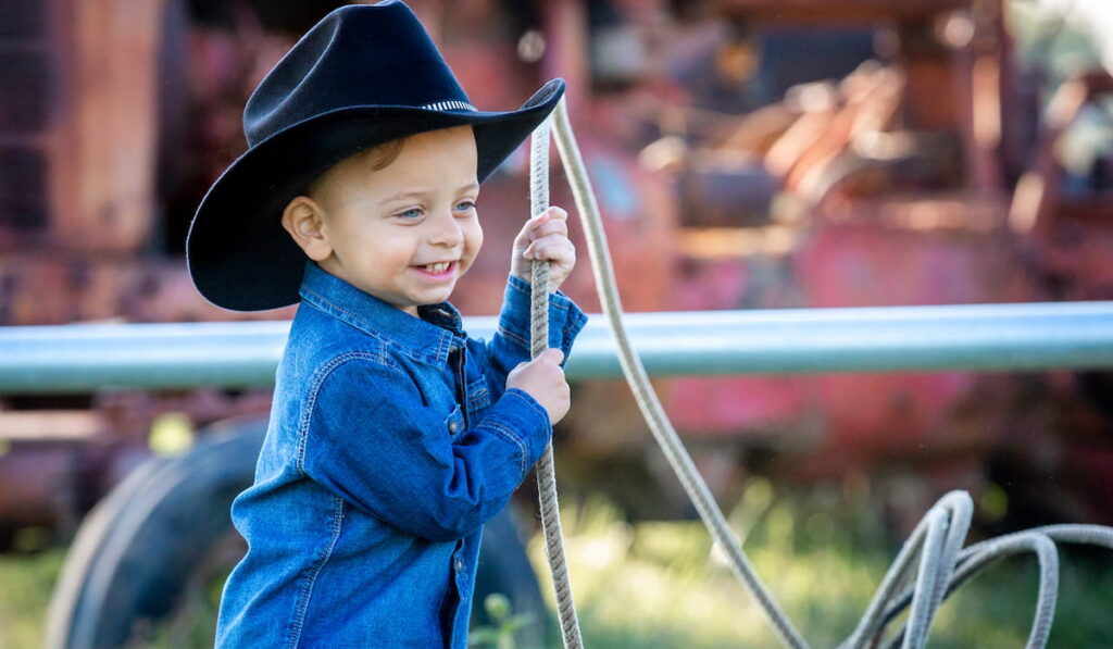 Little boy in a black felt cowboy hat and denim holding a lasso
