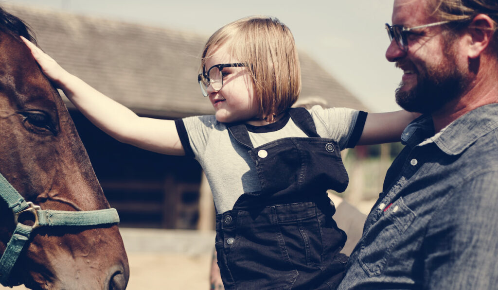 Little girl with her dad petting a horse