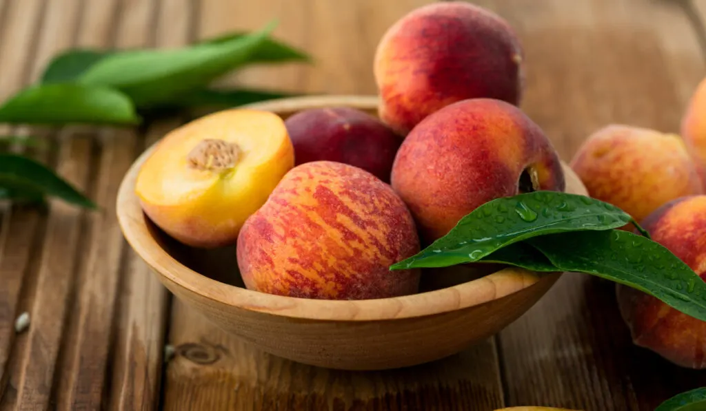 Peaches with leaves in a wooden bowl