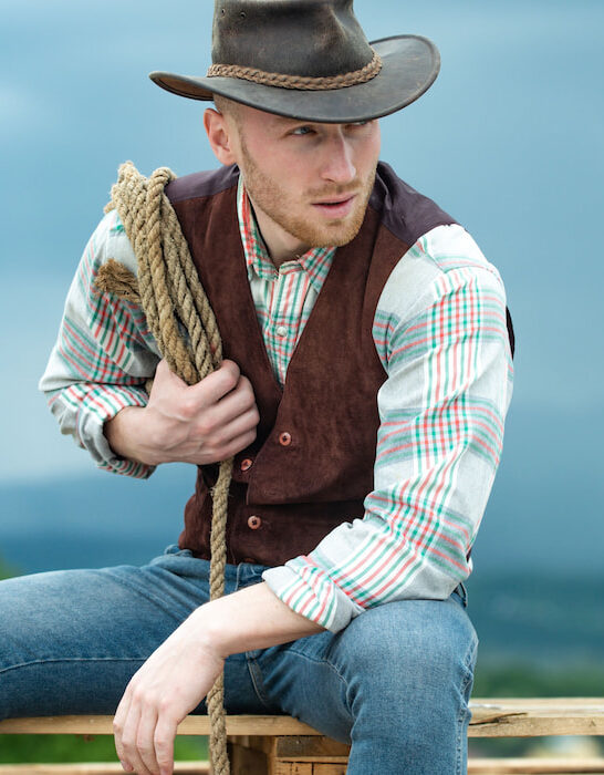 Portrait-of-a-cowboy-sitting-outdoor-holding-his-lasso-rope-and-wearing-vest