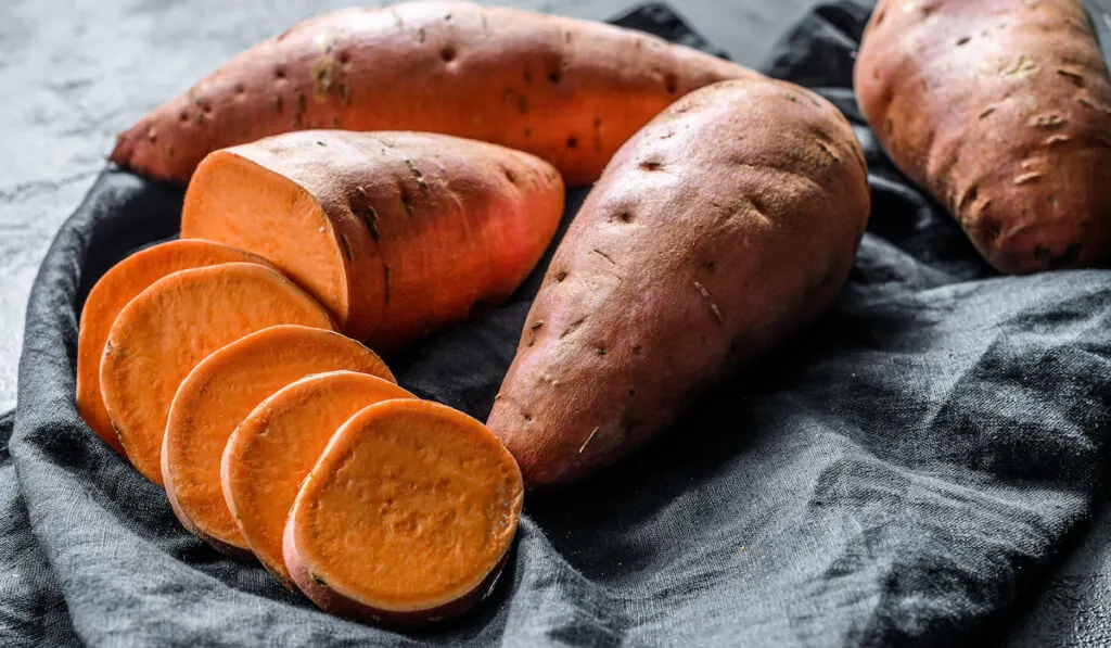 Raw sweet potatoes on black cloth background