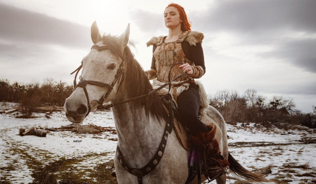 Viking girl with grey horse against the background of mountains.