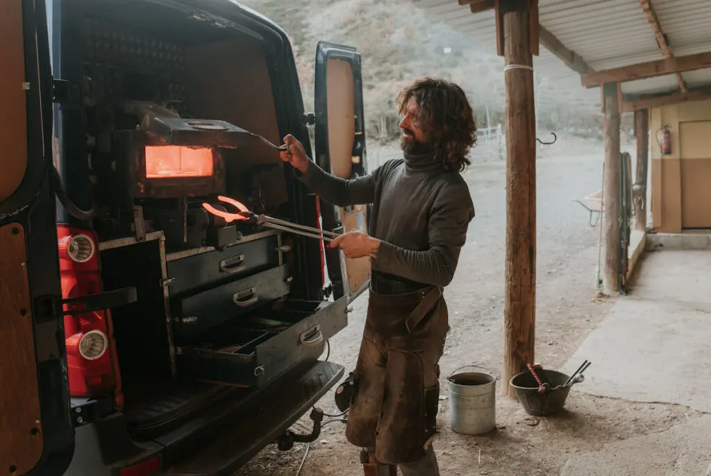 a bearded man taking a horse shoe from the furnace in a farrier's vehicle