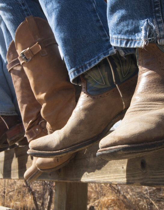 cowboys sitting on a wooden fence, wearing cowboy boots