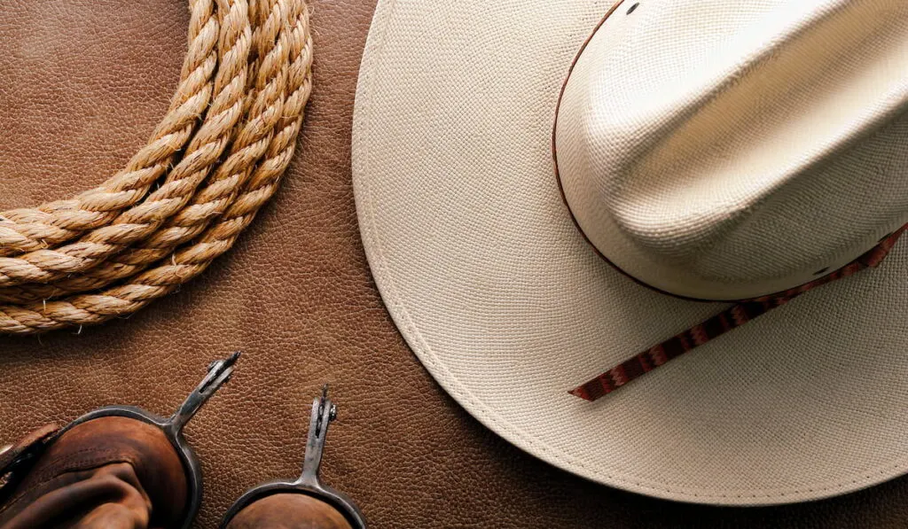 cowboy traditional white straw hat with roping lasso rope and vintage western riding spurs on brown leather boots 