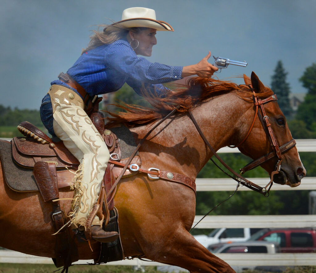 cowgirl with a pistol riding her brown horse during a shooting competition