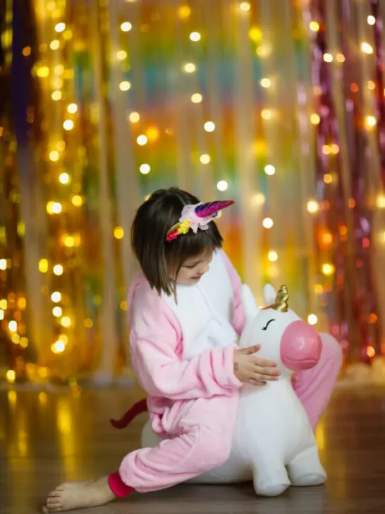 Cute child girl in a soft unicorn costume in pajamas on a colorful background - ee240523