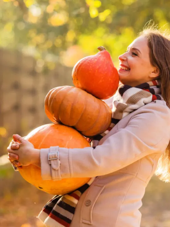 a happy woman carrying three different sized pumpkins
