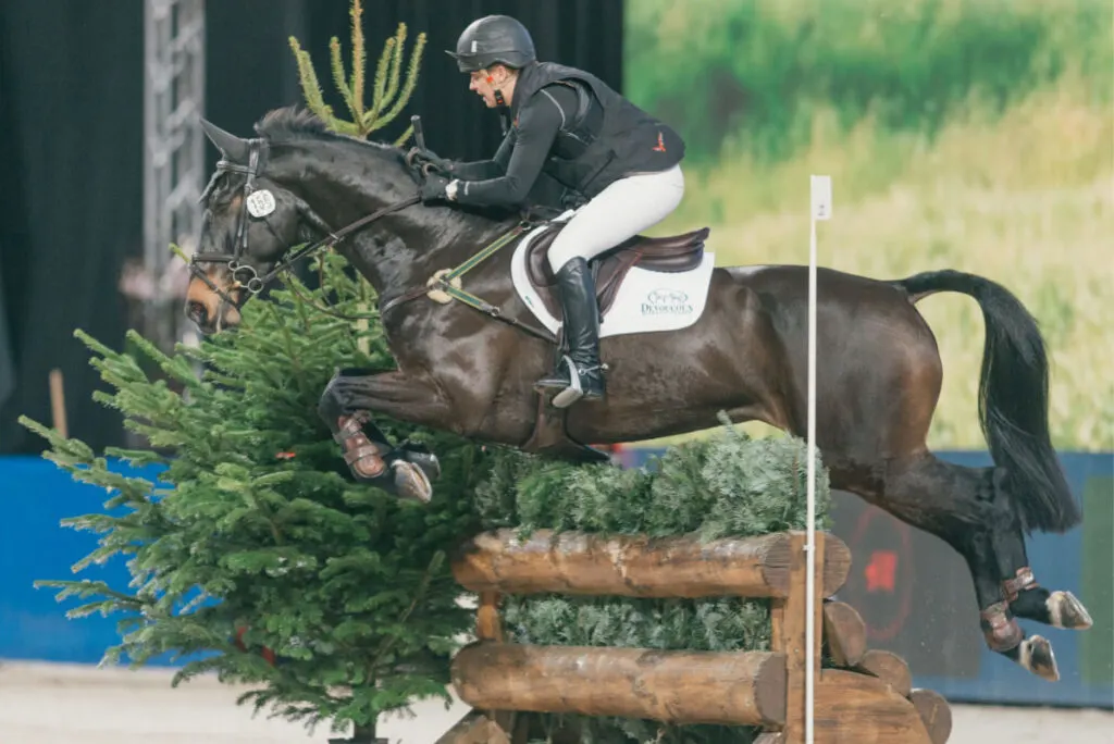 man in white pants riding a horse in a cross country event