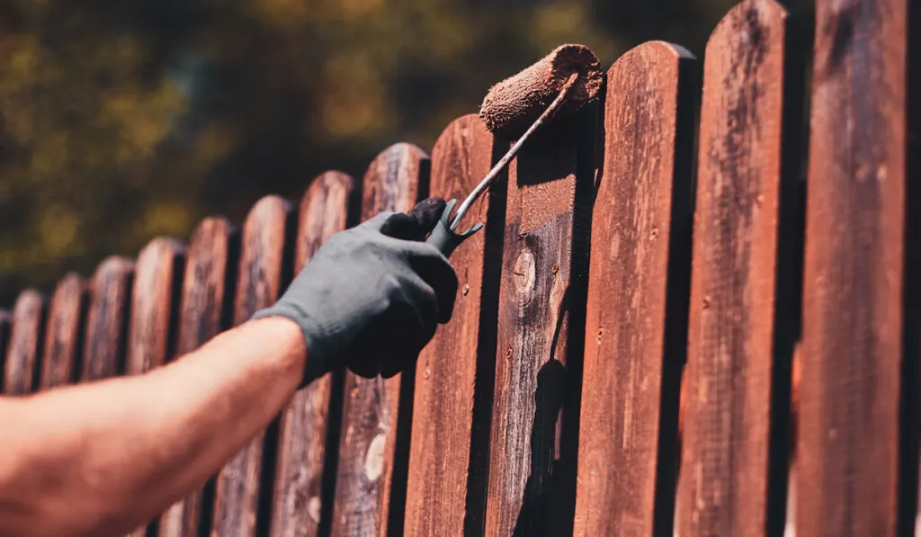 man painting fence brown