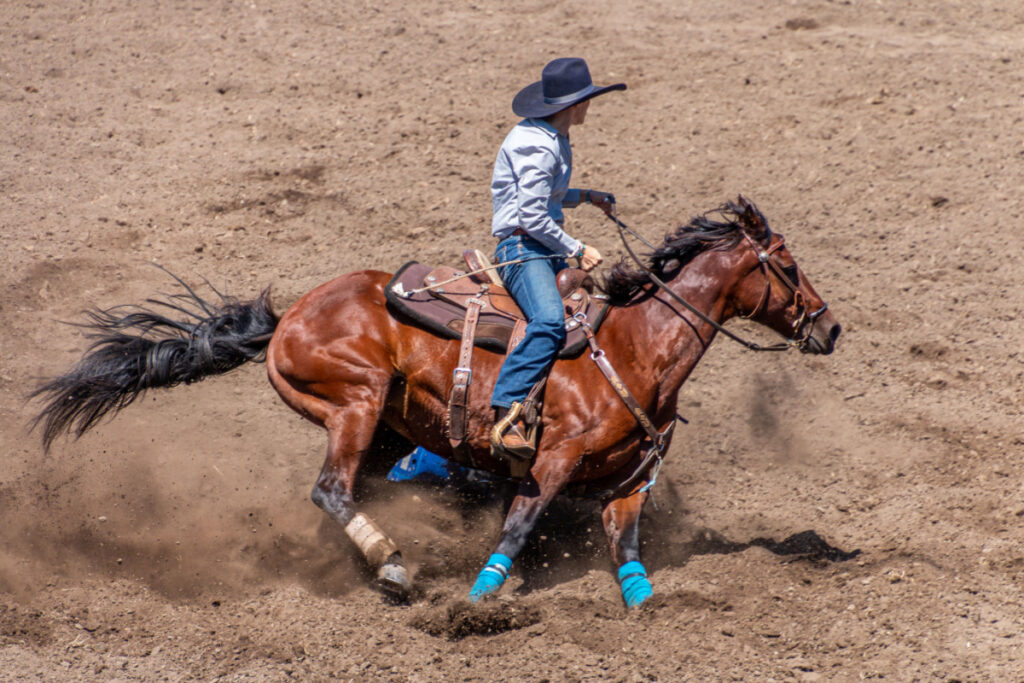 man riding a horse using a barrel saddle on a dusty platform