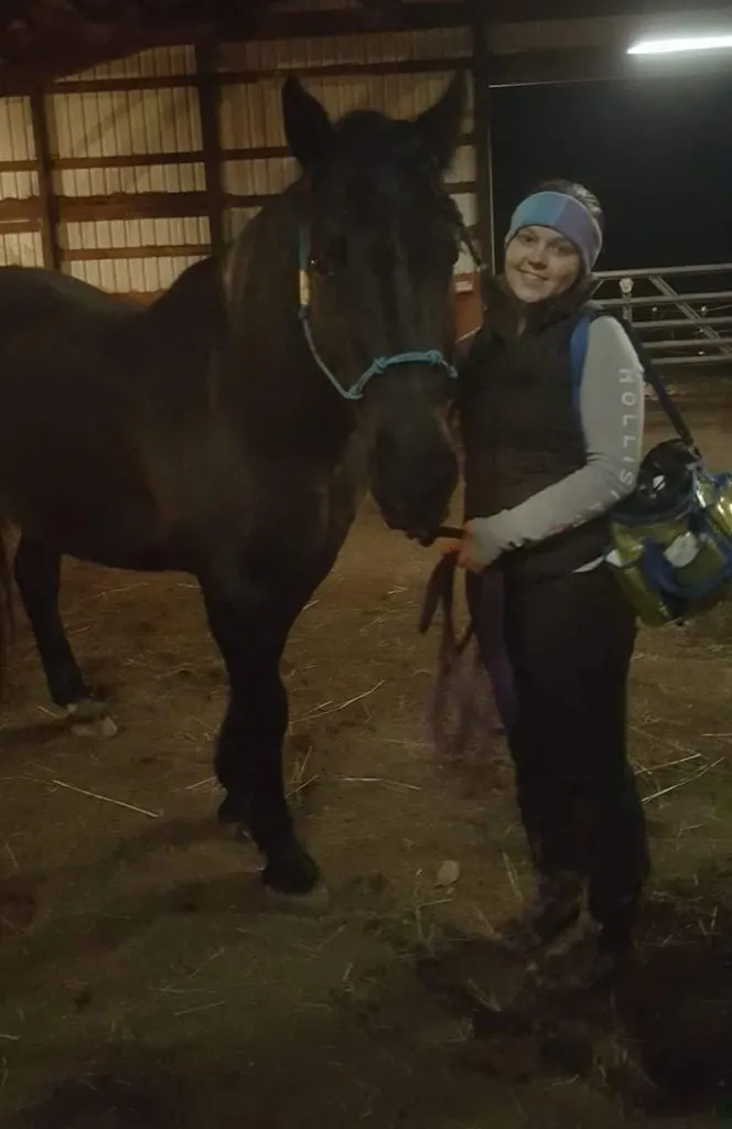 Woman with her horse in the barn at night time