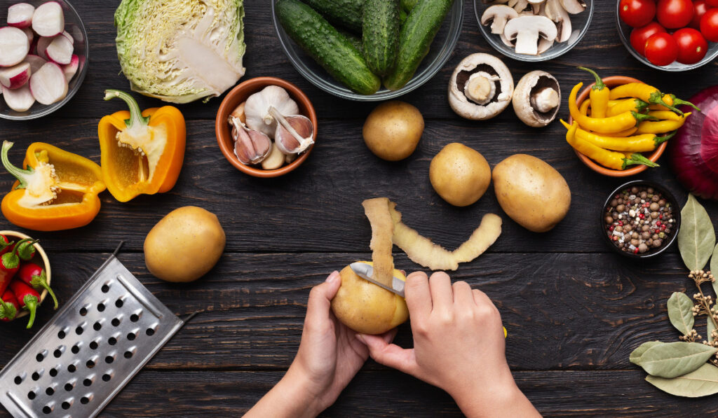 hands peeling potato with other fresh ingredients on the table