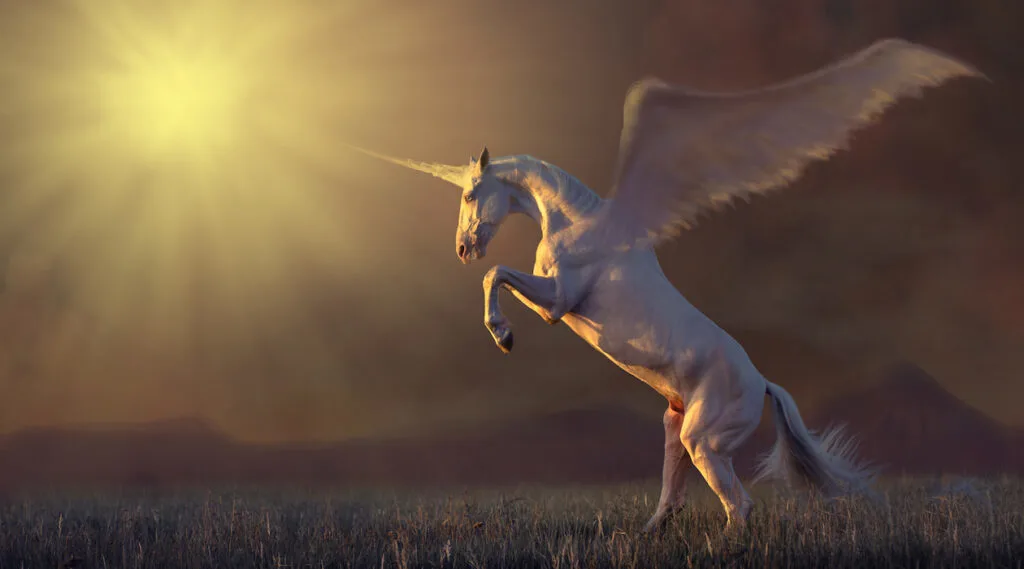 pink unicorn with the wings reared in the grass on mountains background