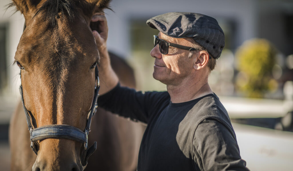 senior man touching his horse for racing 