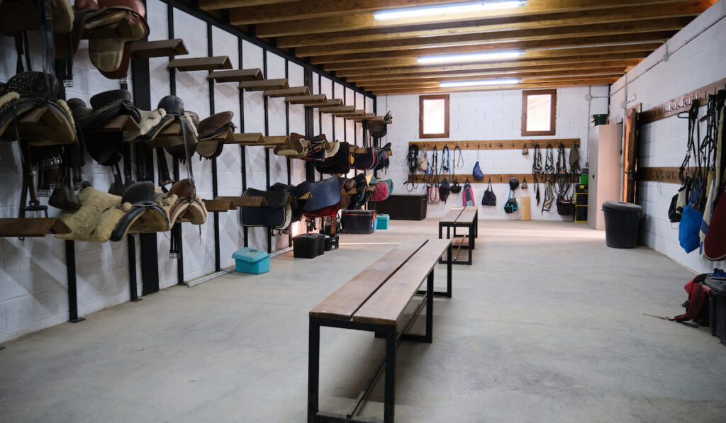 storage room with riding tack, horse saddles and bridles hanging on wall