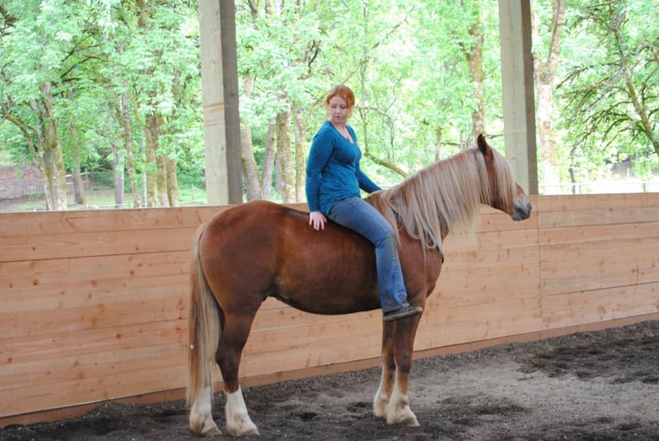 Young woman riding BLM mustang horse in paddock beside wooden fence