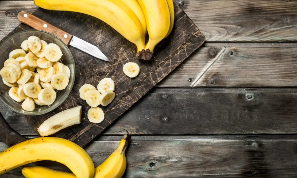 whole and slices of banana on a plate on a black chopping board with a knife