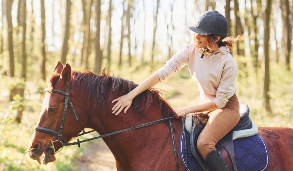 young woman riding a brown horse in the forest 