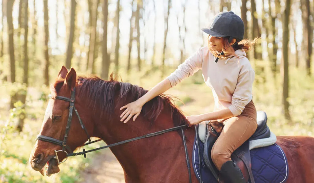 young woman riding a brown horse in the forest