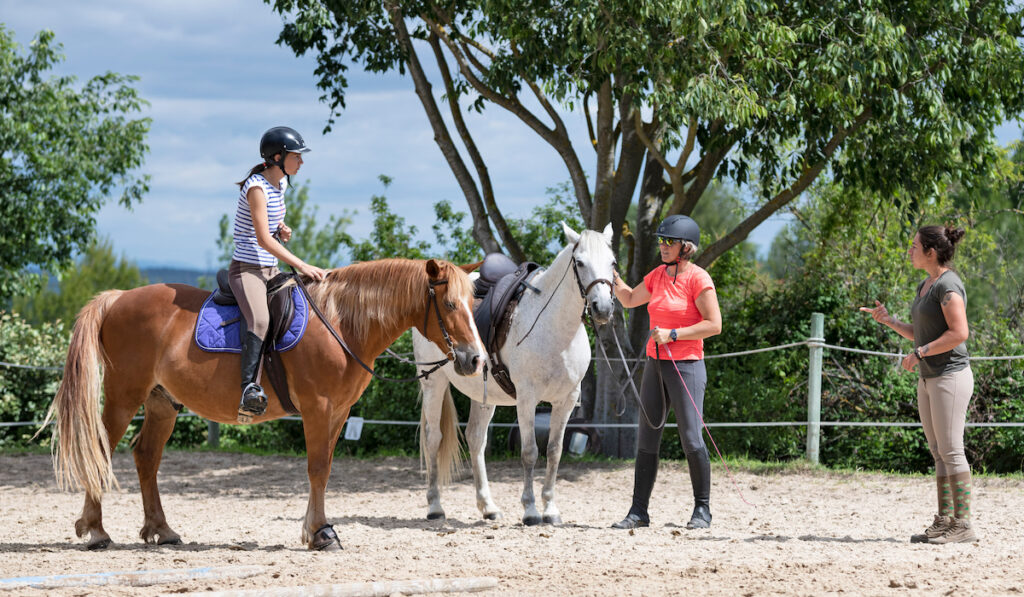young woman riding a horse with riding instructor in equestrian center